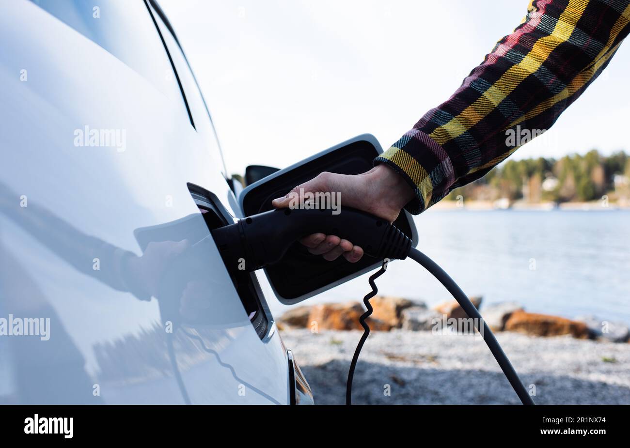 person plugging in an electric car by the sea in Sweden Stock Photo