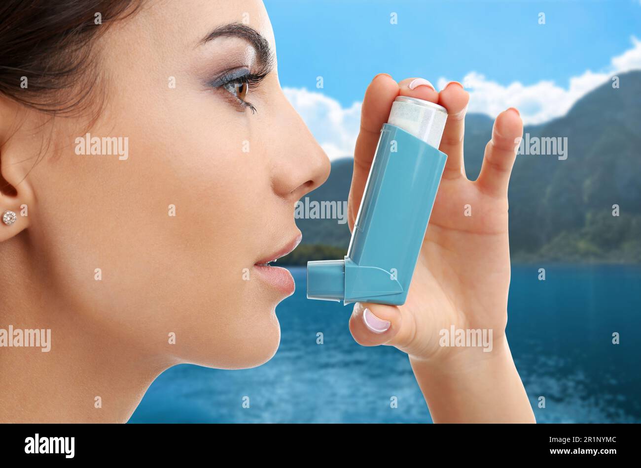 Woman using asthma inhaler near lake. Emergency first aid during outdoor recreation Stock Photo