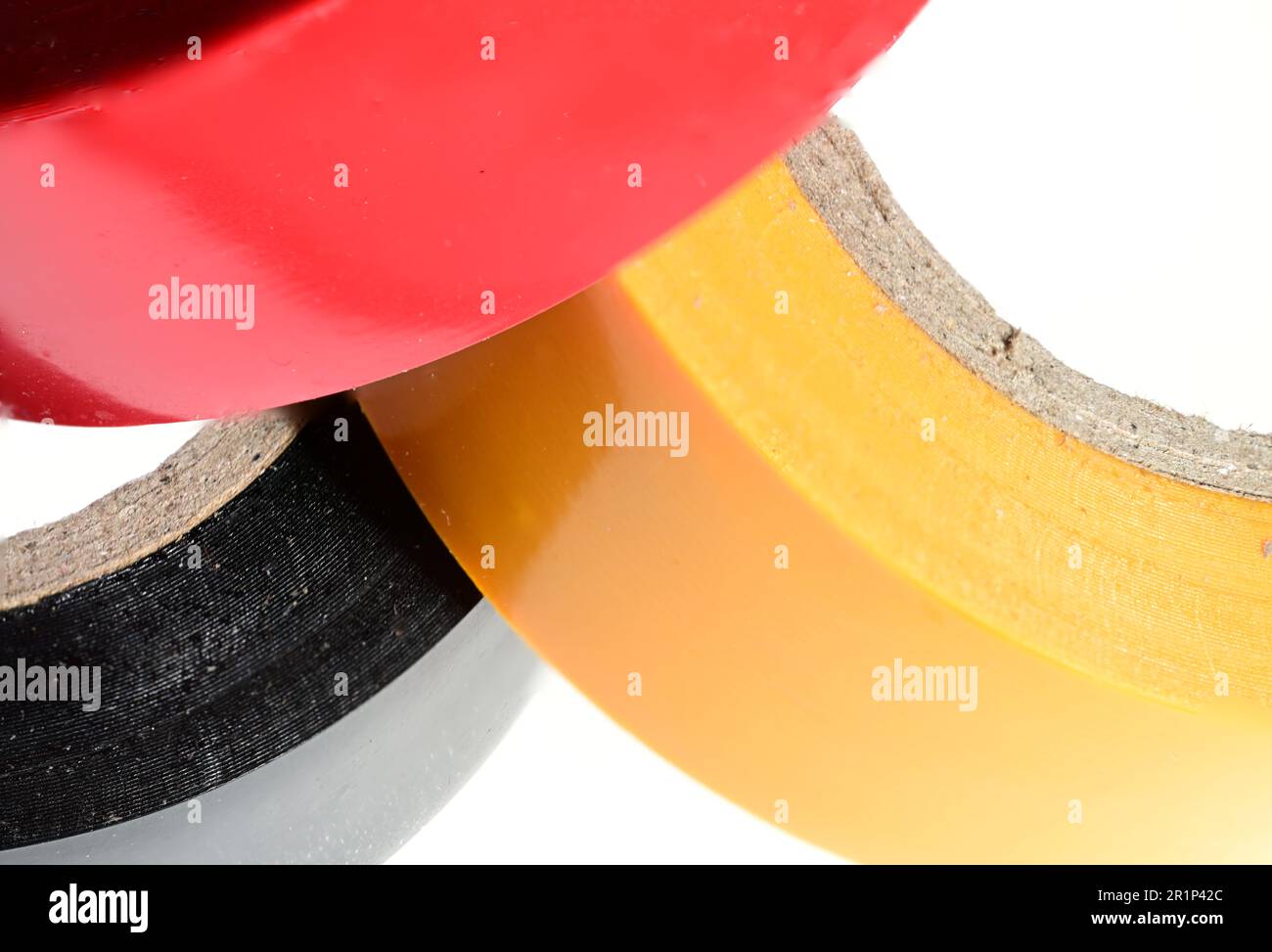 Extreme closeup partial view of three stacked multicolored yellow black red rolls of electrical tape duct tape tape on white background as a concept f Stock Photo