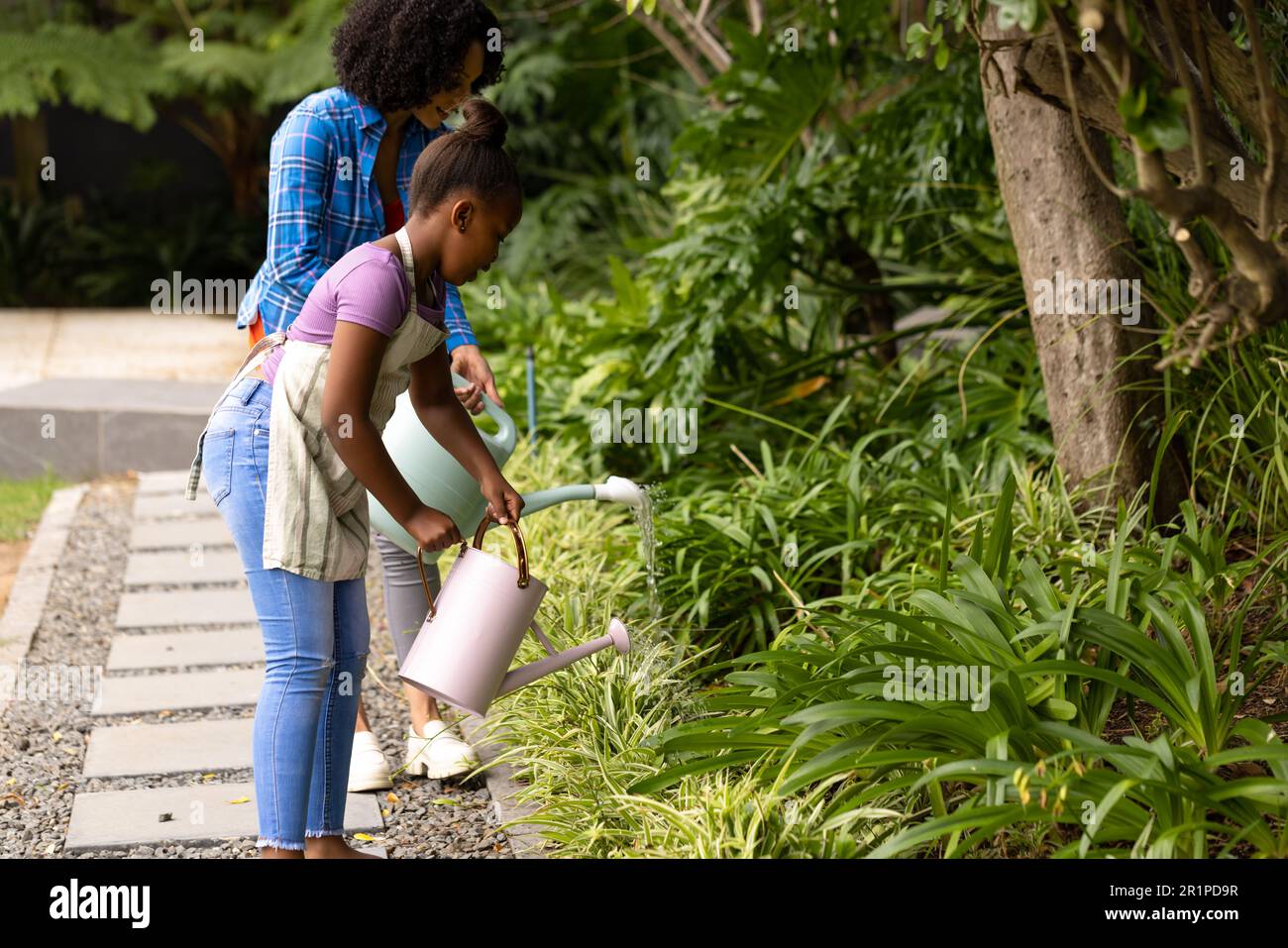 Happy african american mother and daughter watering plants together in ...