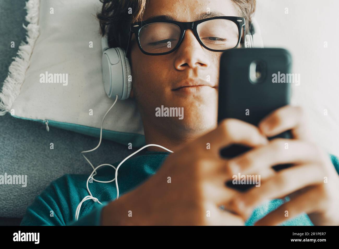 Serene young boy chatting and writing on mobile phone at home laying at bed. One teenager having relax indoor with cell smartphone app playing activity. Online dating modern teenager social media Stock Photo