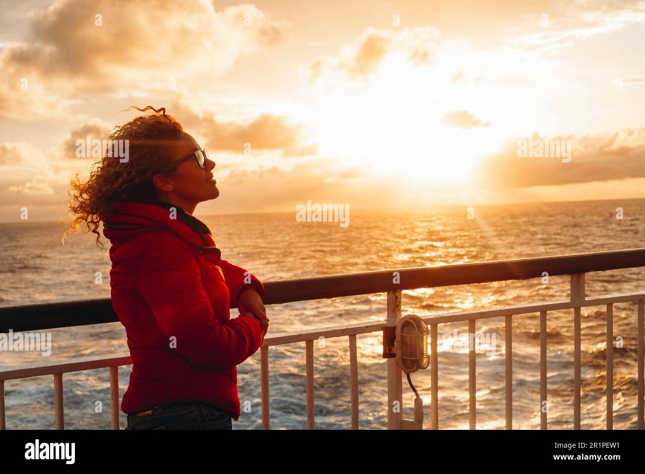 People enjoying travel and adventure lifestyle. One woman on ferry ship boat enjoy sunset sunlight colour smiling and relaxing. Tourist on the ocean transport. Summer trip vacation. Sea surface. Stock Photo