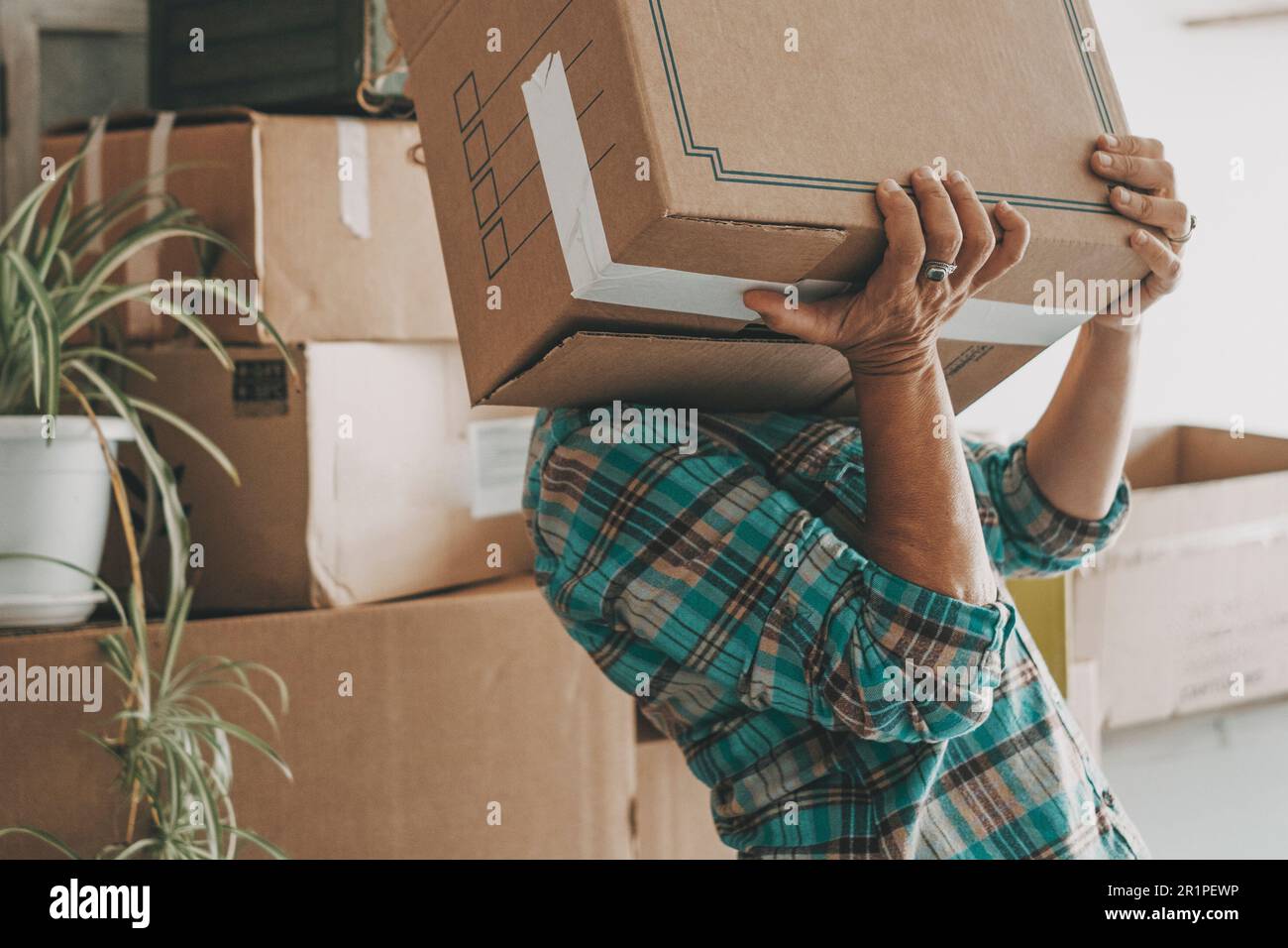 One woman lifting up heavy cardboard box during relocation moving house activity alone. Mortgage. New beginnings adventure female people single lifestyle. Changing life. Home indoors lifestyle people Stock Photo