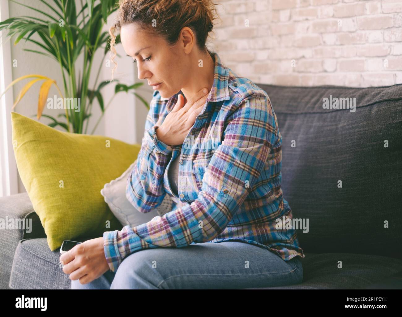 Pressure in the chest. Close-up photo of a stressed woman who is suffering from a chest pain and touching her heart area. People health bad condition and fear. One female touching chest worried Stock Photo