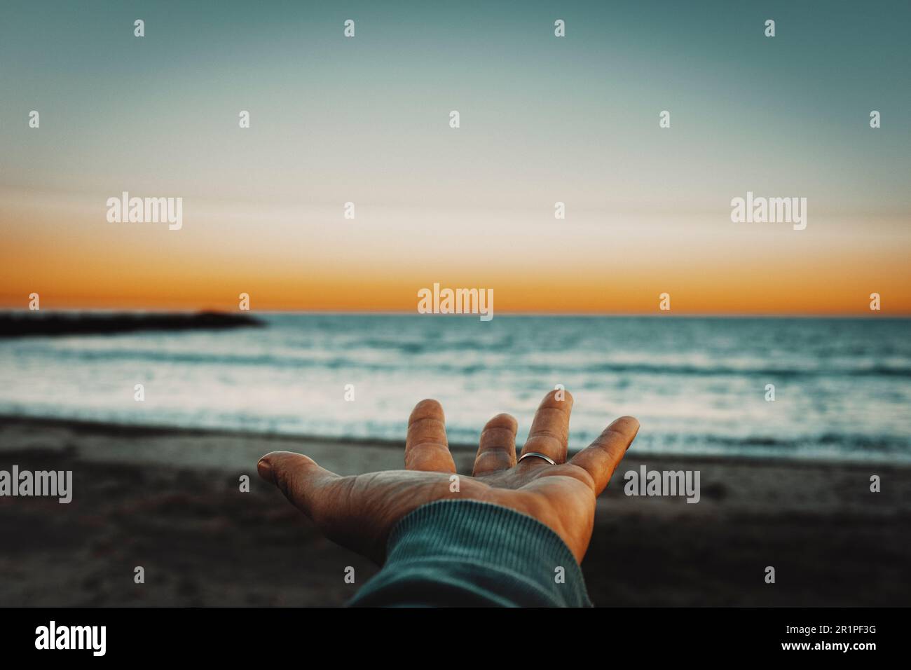 Pov of man hand opened and beautiful sunset lights with ocean and sky in background. Focus in foreground. Concept of mankind and nature. People and travel adventure lifestyle. Feeling. Love. Sea. Stock Photo