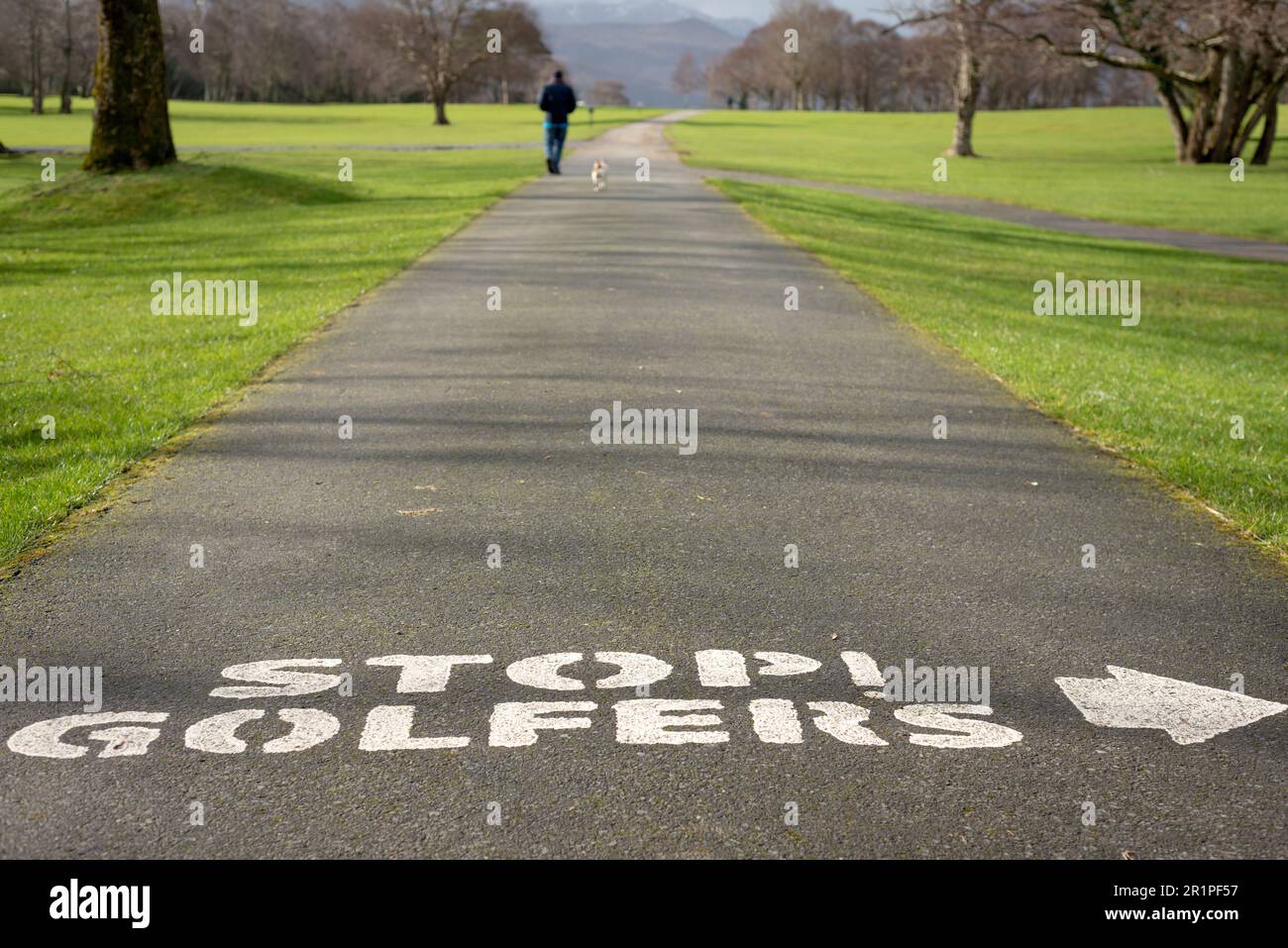 Man with a dog walking on golf course alley with Stop Golfers warning text at the Killarney Golf and Fishing Club, County Kerry, Ireland Stock Photo