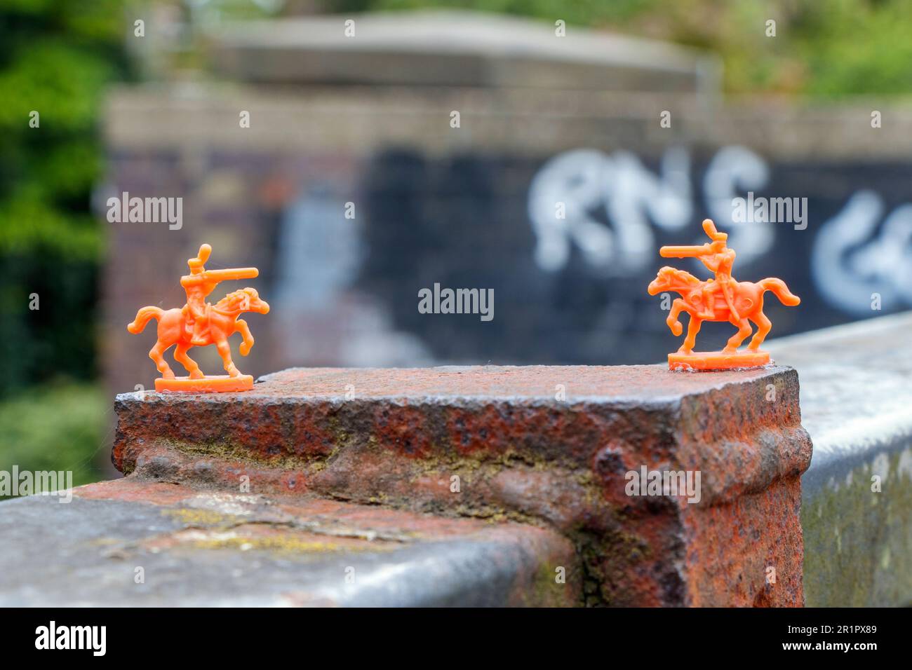 Miniature orange plastic toy soldiers glued to a bridge parapet on Parkland Walk mature trail in North London, UK Stock Photo