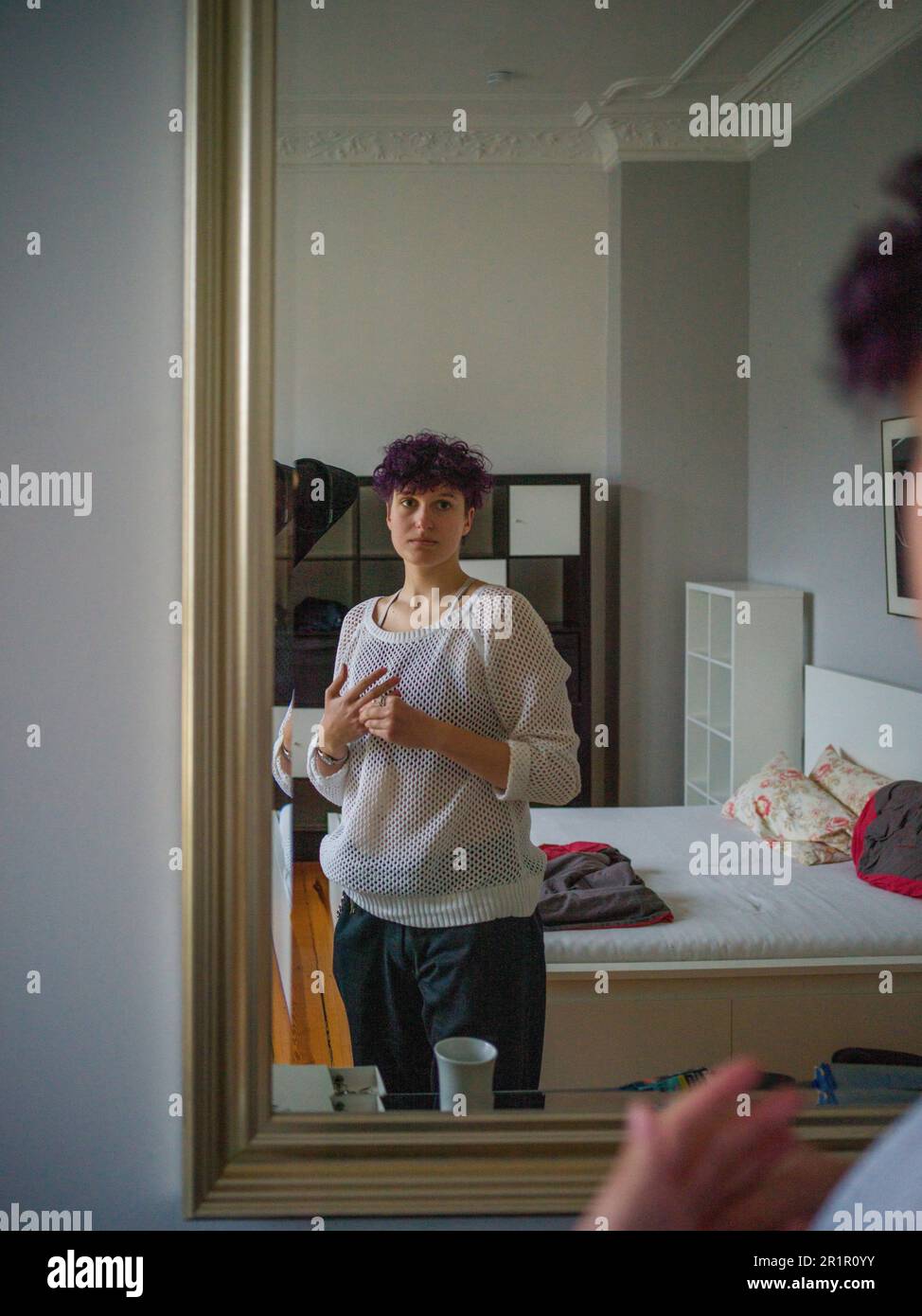 Non-binary person in front of mirror in living room Stock Photo