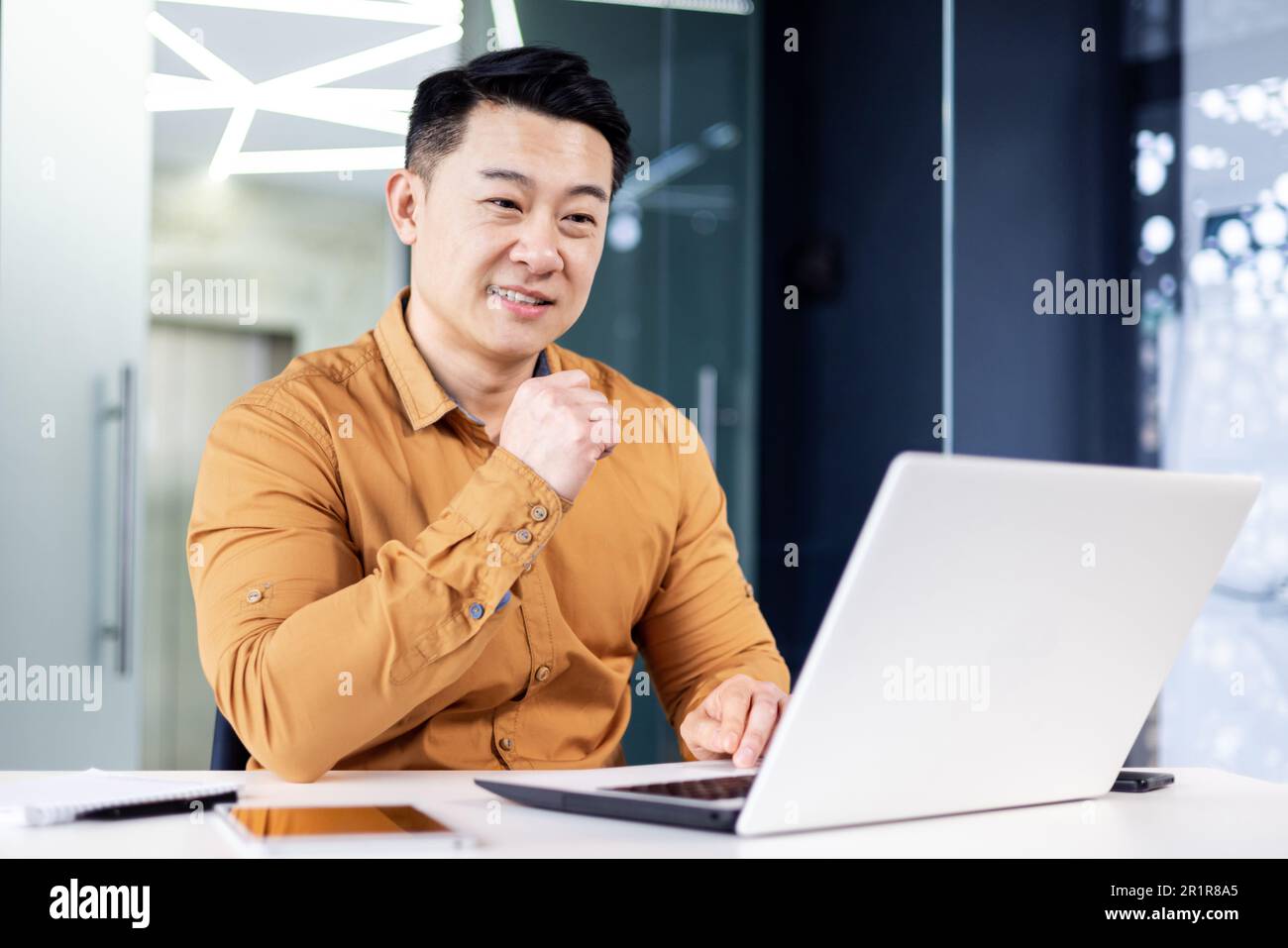 Cheerful and smiling Asian man working inside office, businessman in shirt and glasses using laptop, engineer developer programmer typing code programming software Stock Photo