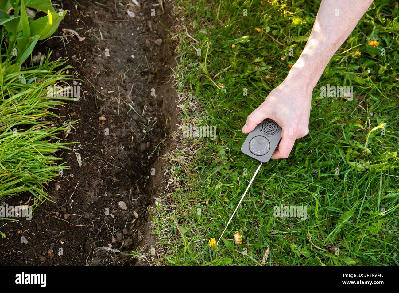 How do you find a break in a robotic mower perimeter wire. Person man hand using AM radio interference signal to locate broken part of the wire. Stock Photo