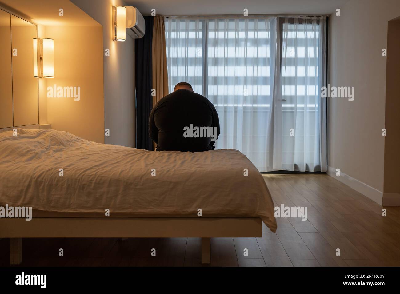 Sad fat lonely man sitting on bed in hotel, suffering from divorce, has no friends, mental disorder Stock Photo