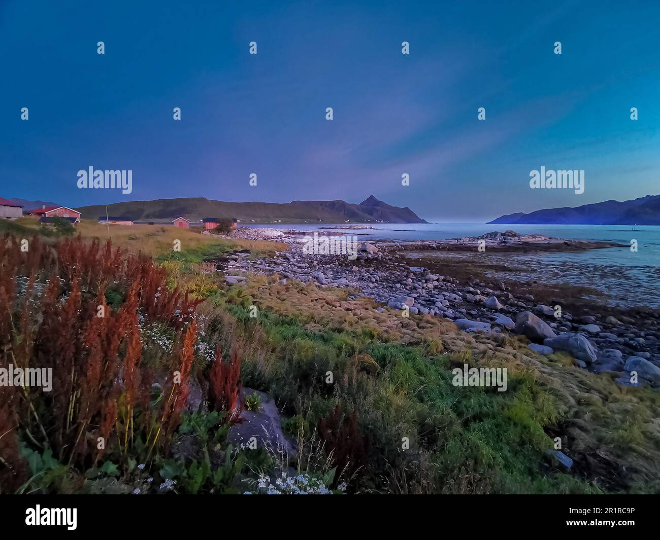 Rocky beach at dusk with houses in the distance, Lofoten, Nordland, Norway Stock Photo