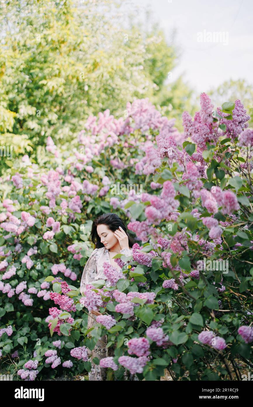 Young pretty brunette woman walks in garden and enjoys with closed eyes ...
