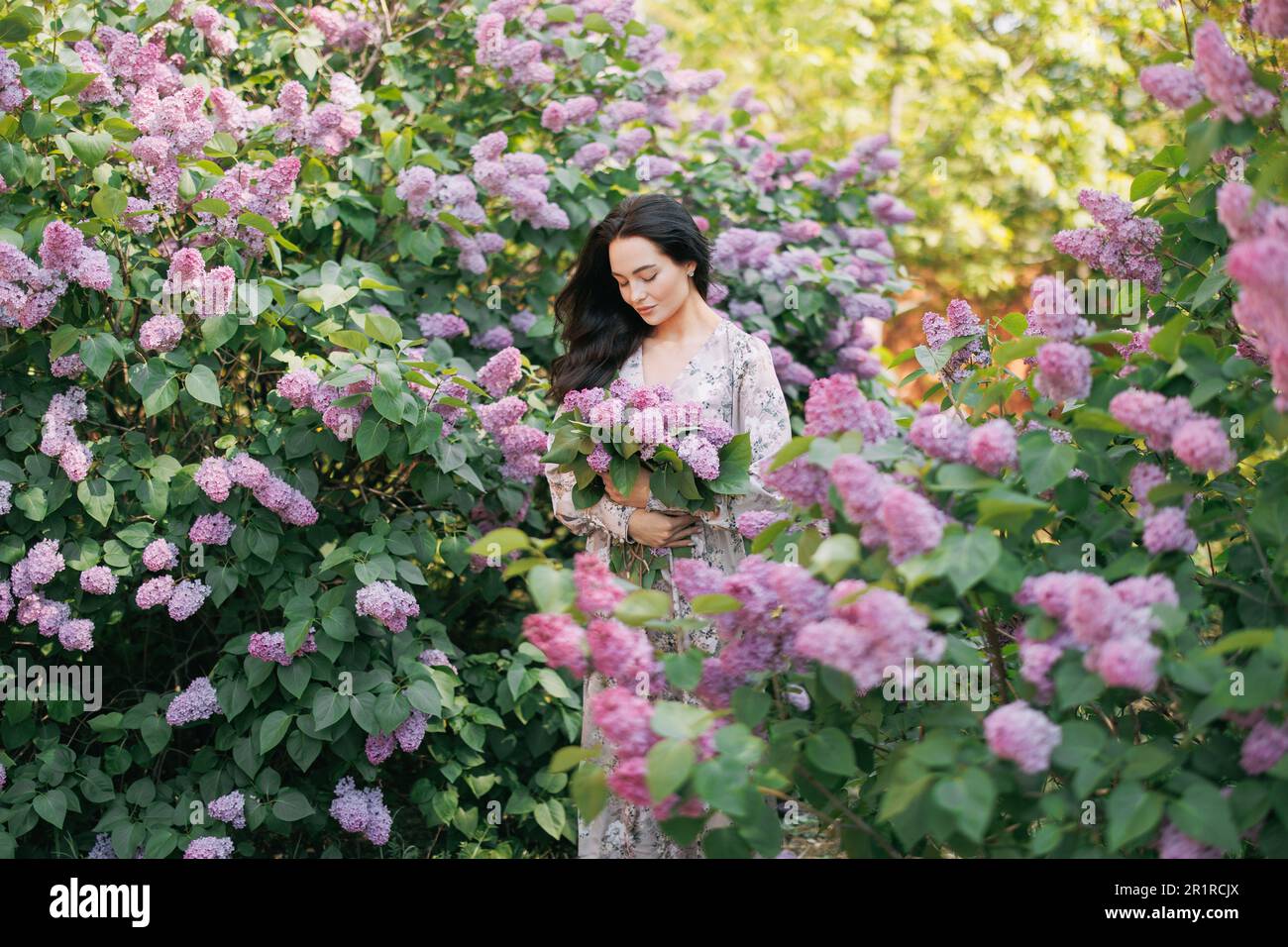 Young pretty brunette woman walks in garden with bouquet in her hands ...