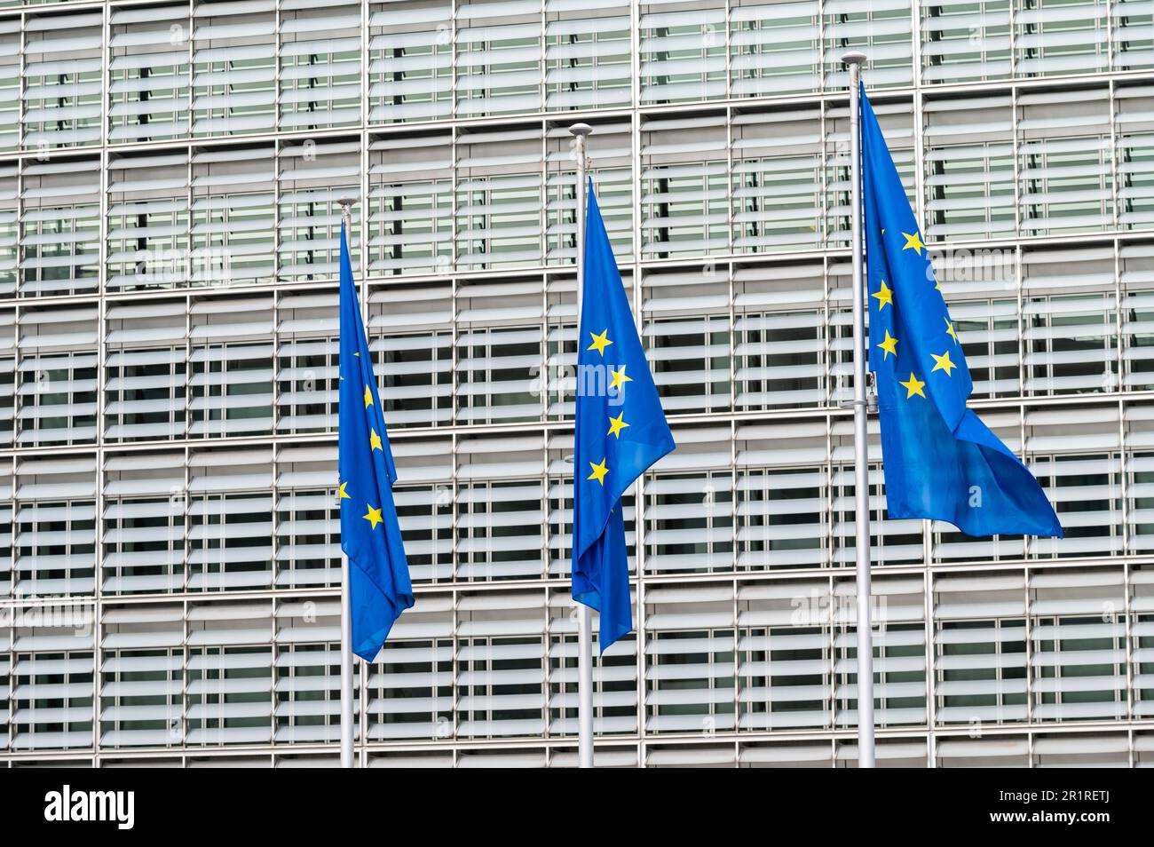 Brussels European Quarter, Belgium - March 15, 2023 - Three European flags with the Berlaymont building in the background. Stock Photo