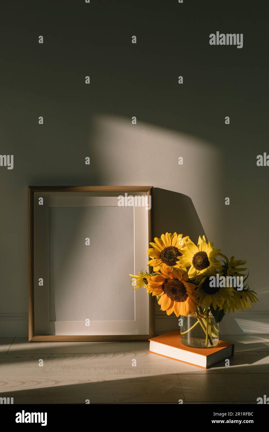 Vase of sunflowers on a hardback book next to a blank picture frame in the sunlight Stock Photo