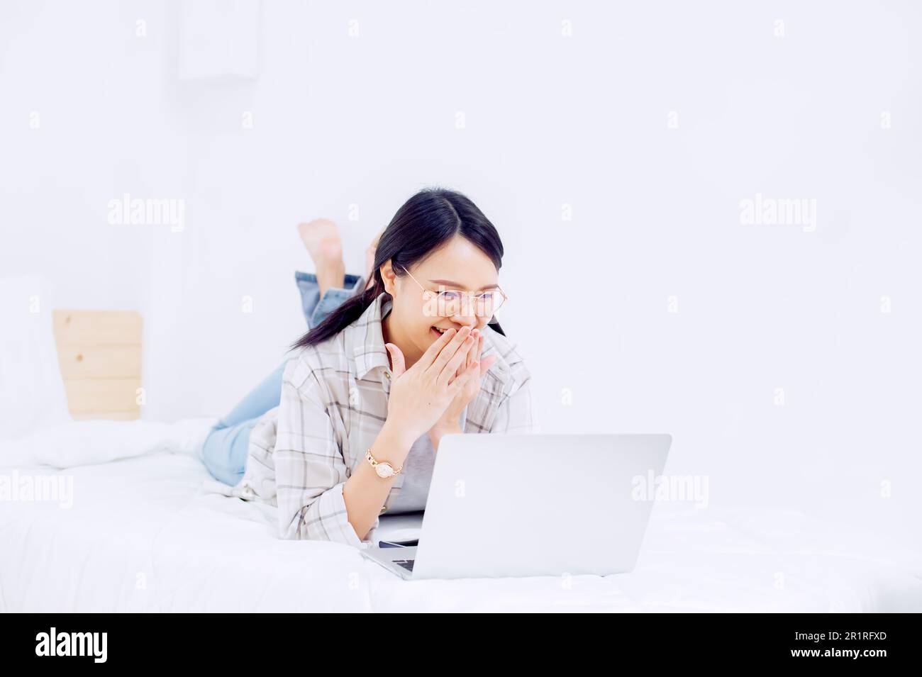 Smiling woman lying on her bed making a video call on her laptop computer Stock Photo
