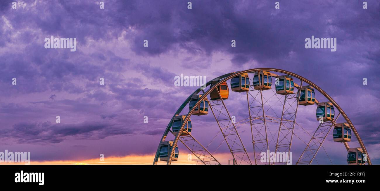 Helsinki, Finland. Very Peri Cloudy Sky Above Ferris Wheel. Light Violet Colors. Bright Dramatic Yellow Light Purple Sky. Stock Photo