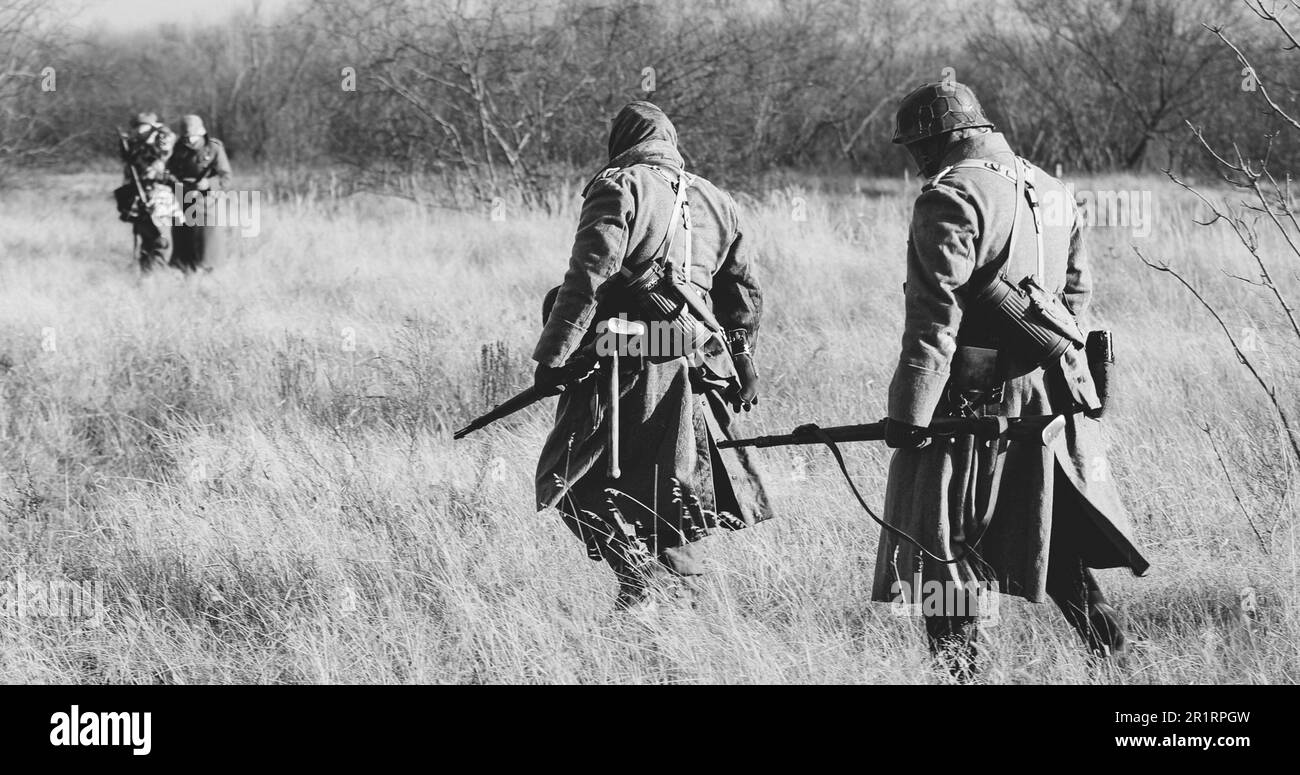 Re-enactors Dressed As German Infantry Soldiers In World War II Marching Walking Along Meadow In Cold Autumn Day. Black And White Colors. Stock Photo