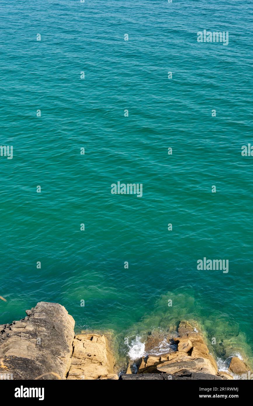 Looking down to rocks and blue pristine sea. Ocean background with copy space Stock Photo