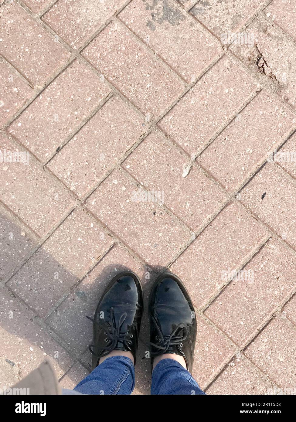 Top view of the legs, shoes, girls feet, women in patent leather shoes on the background of a stone brown red concrete square paving rectangular tile. Stock Photo