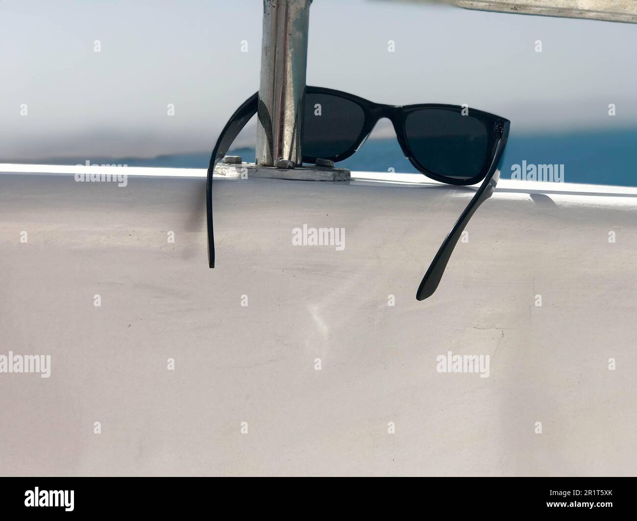 Black plastic sunglasses hang on an iron railing on a yacht against the backdrop of the sea