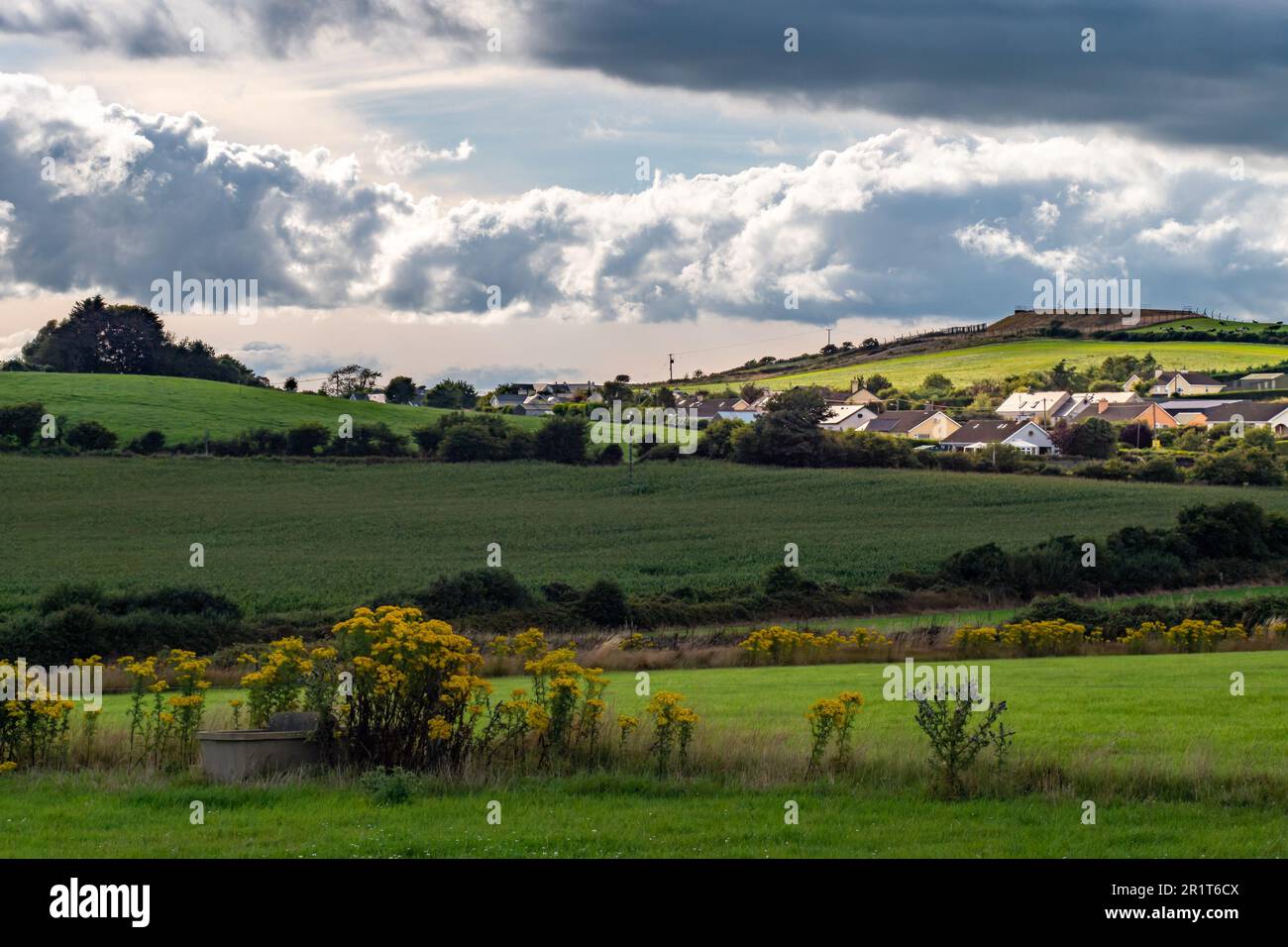 Sky with cumulus clouds over a Irish village on evening. Irish settlement in County Cork, landscape. European countryside, rustic landscape. Green gra Stock Photo