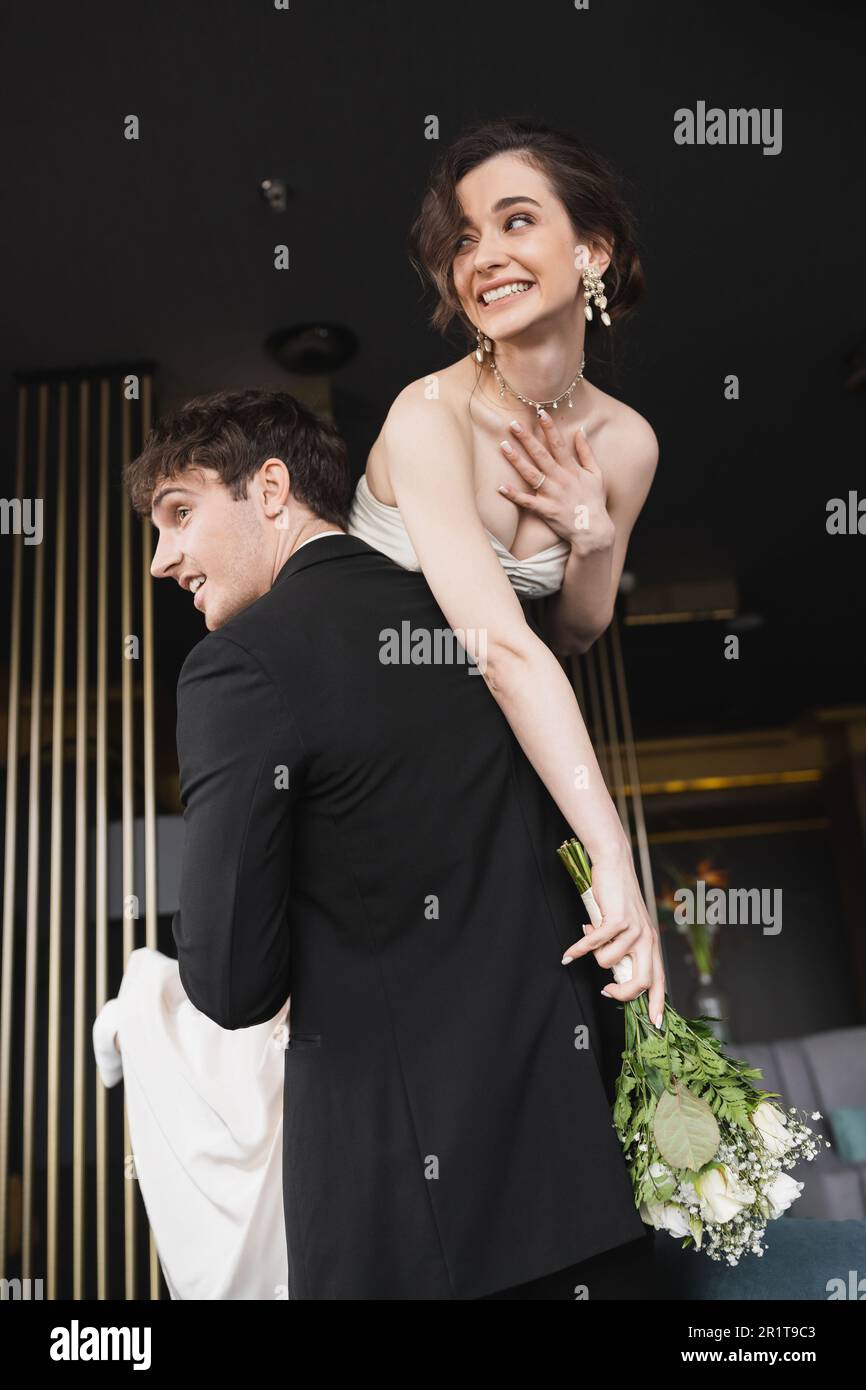 good looking groom in black formal wear lifting cheerful bride with makeup  in white wedding dress holding bridal bouquet of flowers while standing in  Stock Photo - Alamy