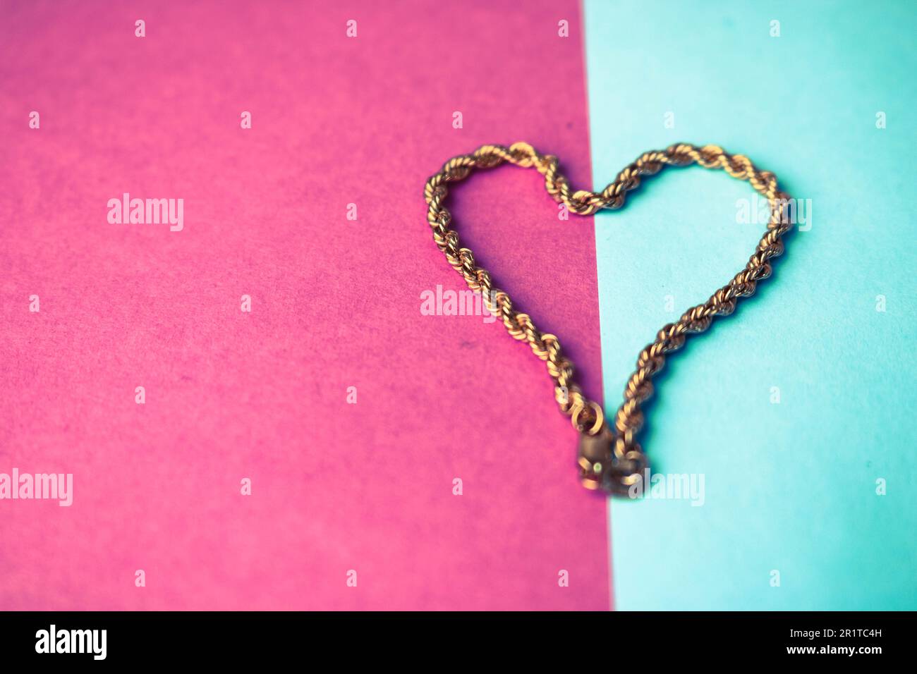Texture of a beautiful golden festive chain unique weaving in the shape of a heart on a pink purple blue background and copy space. Concept: love, mar Stock Photo