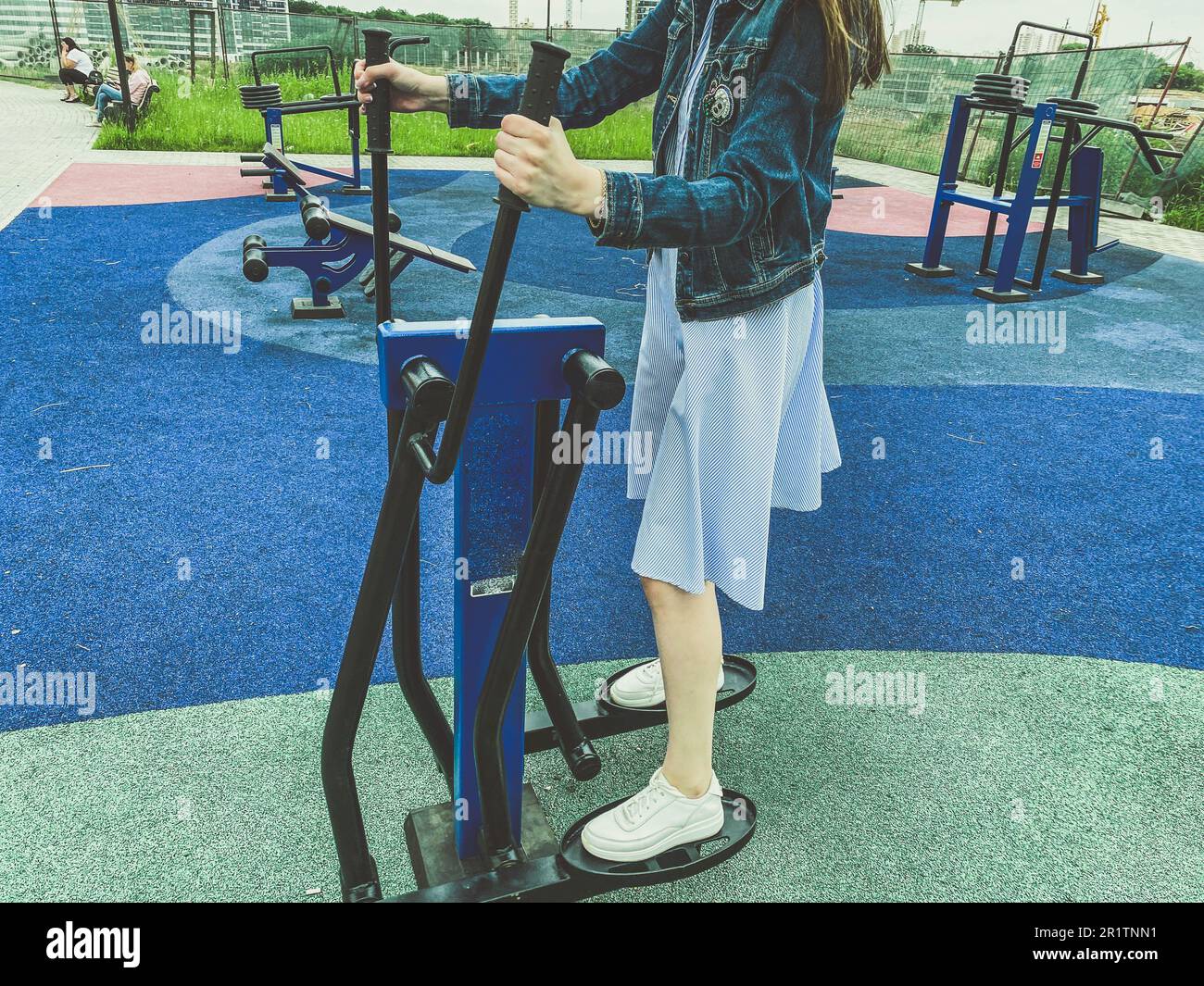 outdoor sports. playground with exercise equipment in the park. a girl in a  dress, jeans and white sneakers on the simulator is engaged in fitness. we  Stock Photo - Alamy