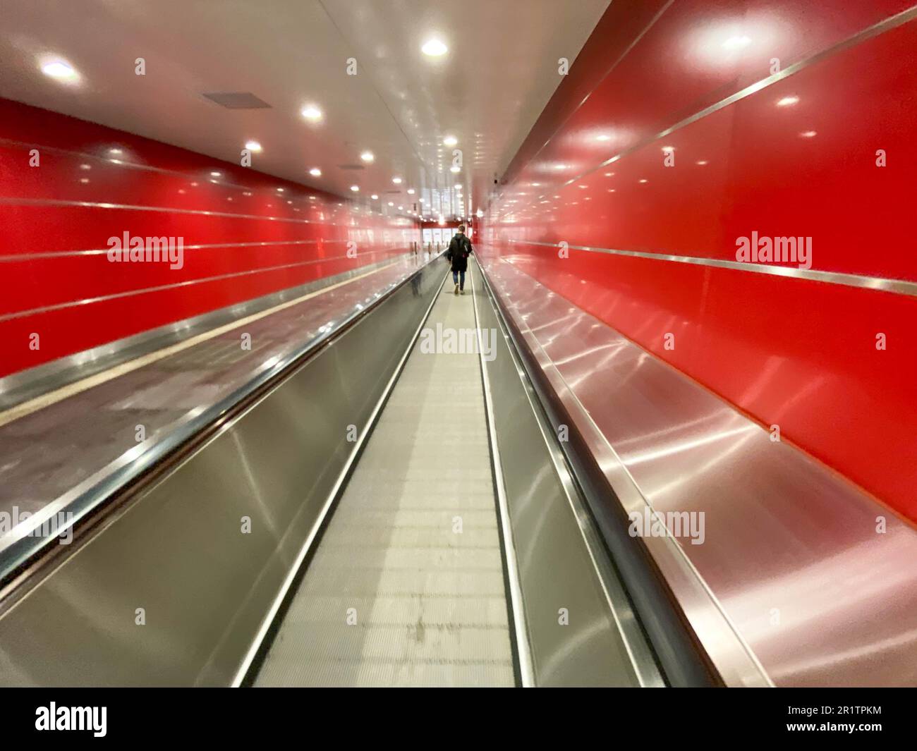 Large red modern long bright underground walkway between metro stations with travel walkers and escalators for quick passage of passengers. Stock Photo