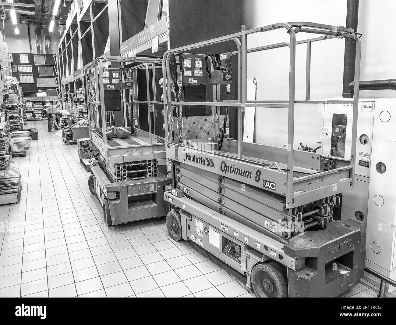 Large yellow mobile hydraulic lift on wheels for lifting and moving people and cargo on racks in a supermarket at the warehouse. Belarus, Minsk, Octob Stock Photo