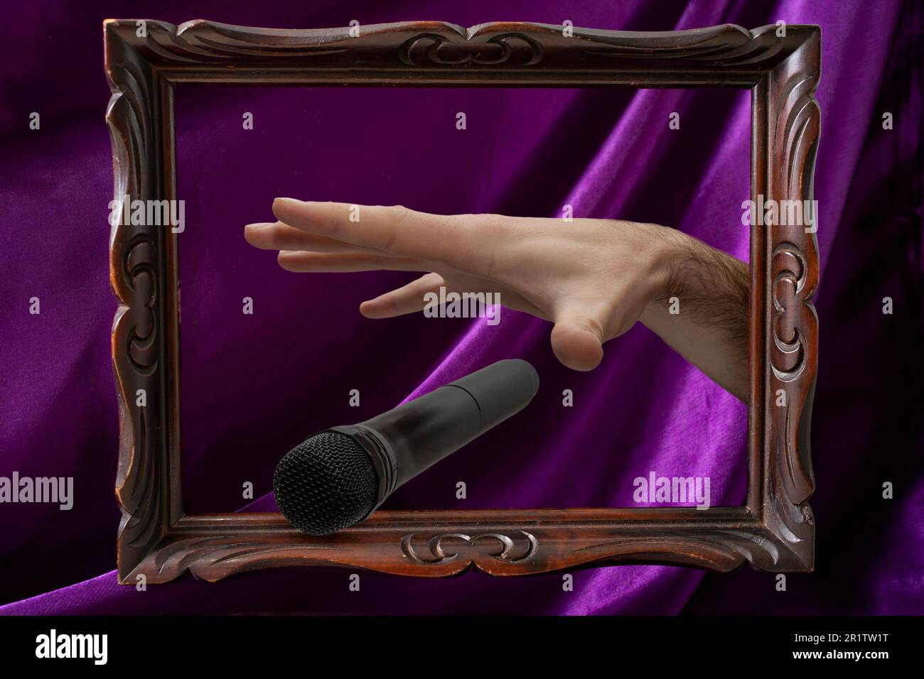 Caucasian male's hand dropping the mic, stretched hand and a microphone coming out of a levitating wooden frame on purple satin background Stock Photo