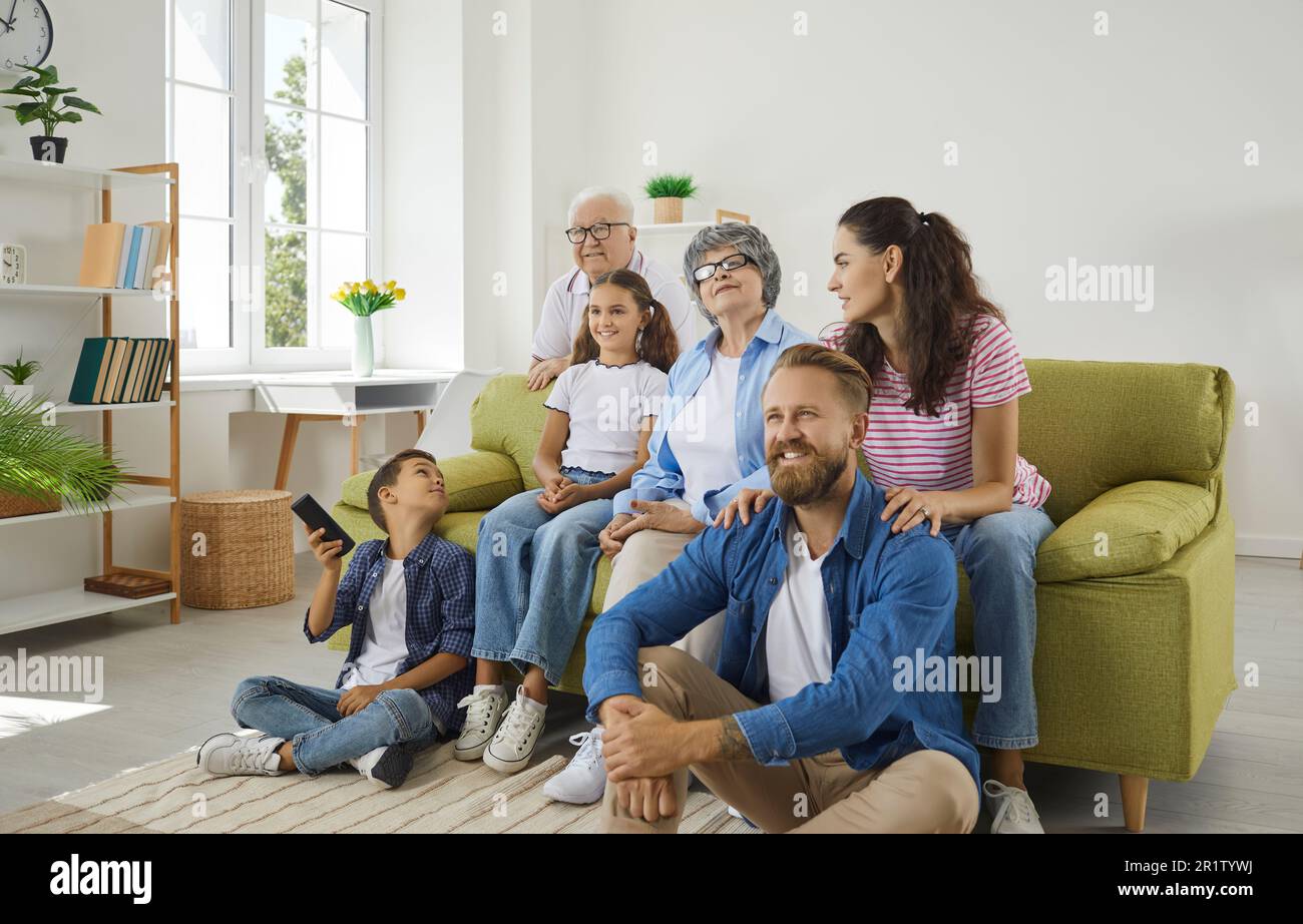 Big happy friendly family grandparents, parents and kids watching TV at home sitting on sofa. Stock Photo