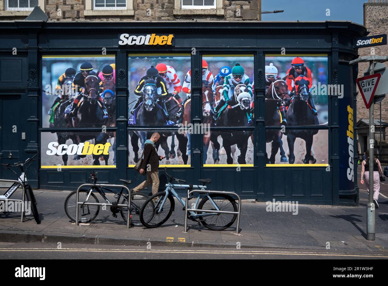 Man looking at his phone as he walks by the window of a Scotbet betting shop in Nicolson Square, Edinburgh, Scotland, UK. Stock Photo