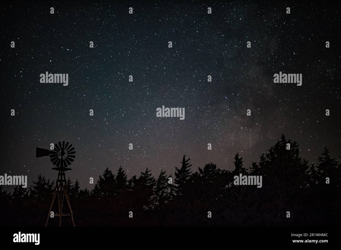 An astrophotography of the night sky taken over a single windmill in ...