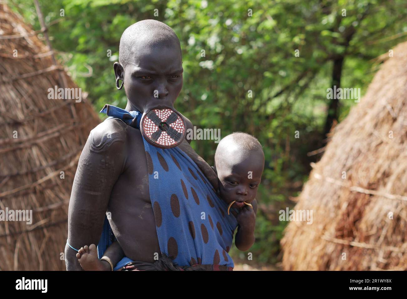 Omo Valley, Ethiopia â€“ 11.17.2022: Woman from the Mursi tribe with large lip plug stands with her baby Stock Photo