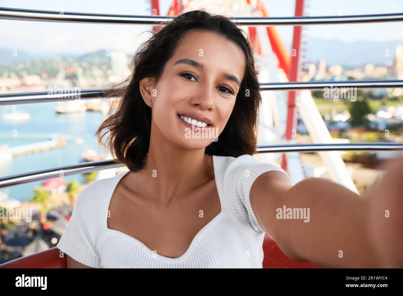Happy young woman taking selfie on Ferris wheel near sea Stock Photo
