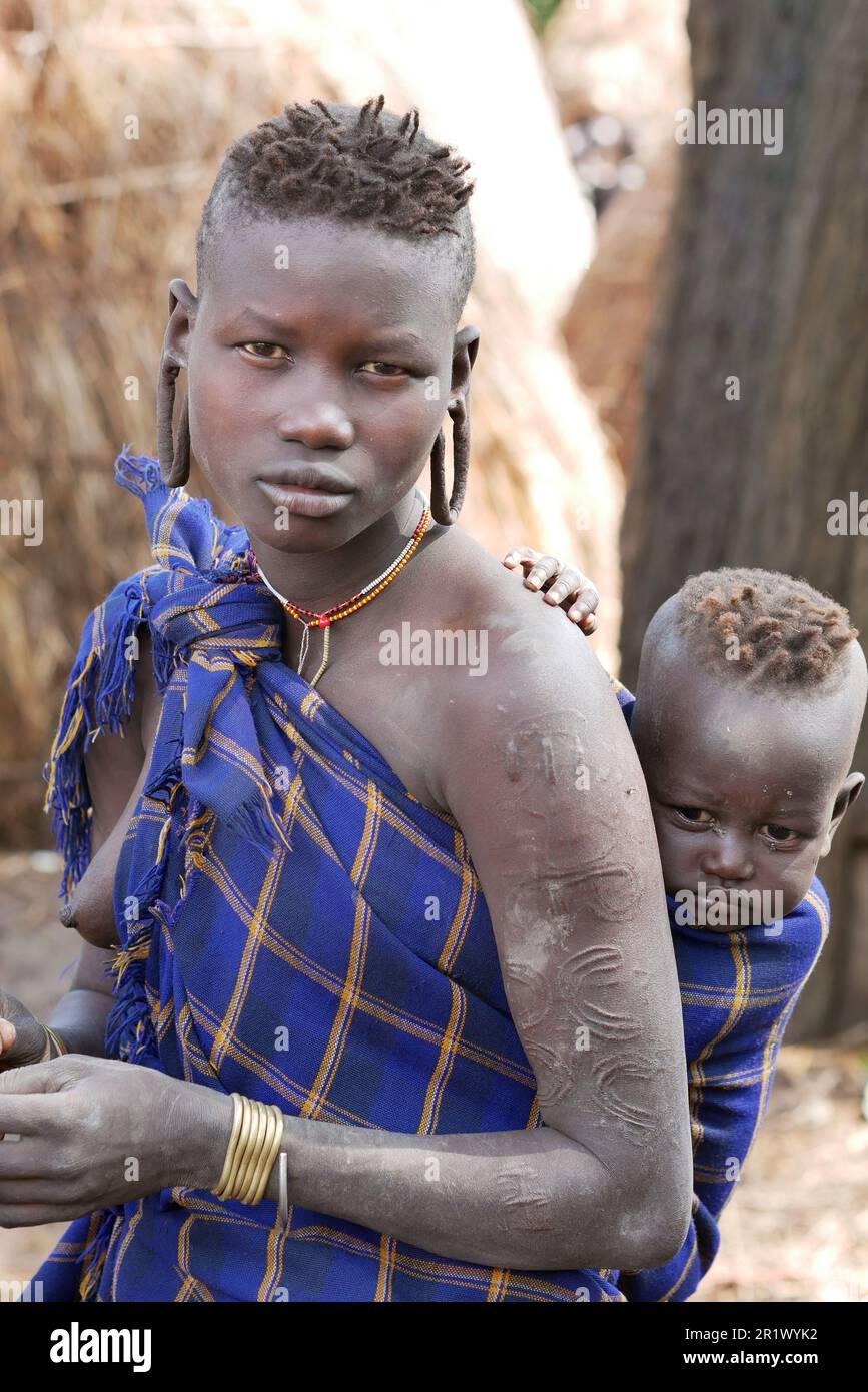 Omo Valley, Ethiopia â€“ 11.17.2022: Woman from the Mursi tribe carrying her baby Stock Photo