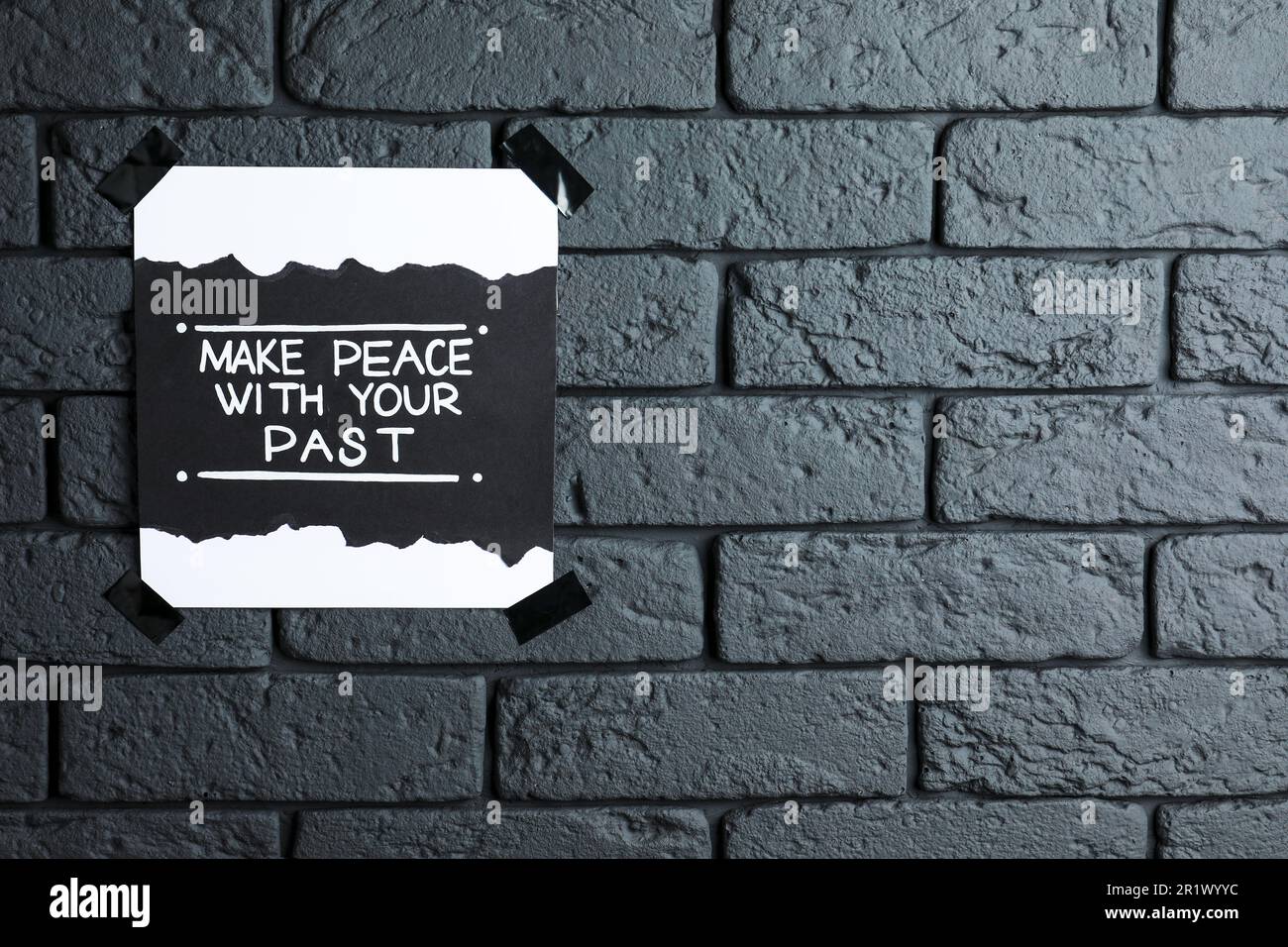 Card with life-affirming phrase Make Peace With Your Past on dark brick wall. Space for text Stock Photo