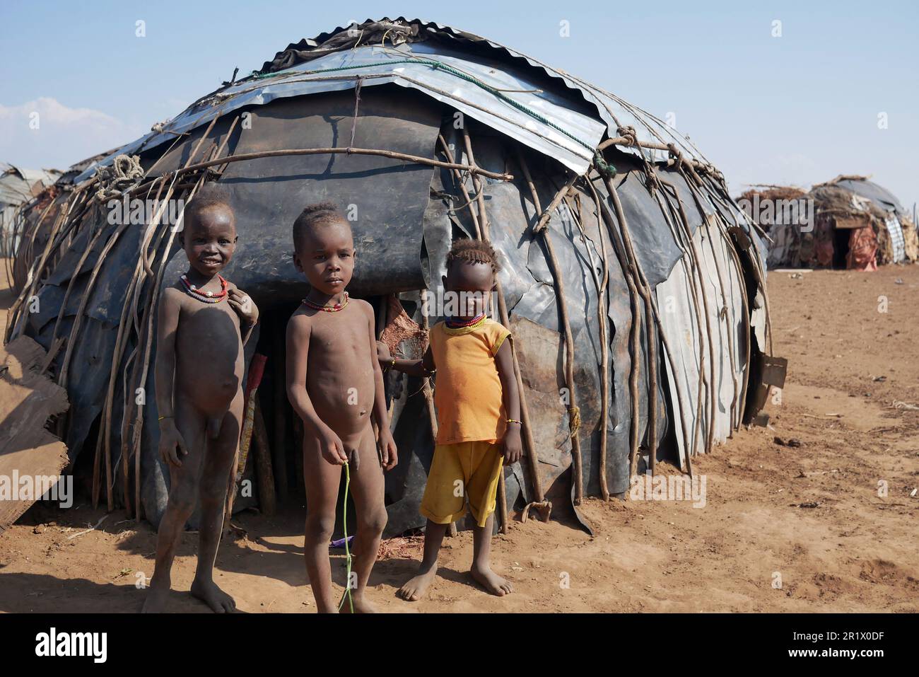 Omo Valley, Ethiopia â€“ 11.18.2022: Young children from the Dassanech tribe stand outside a hut built from metal sheets and sticks Stock Photo