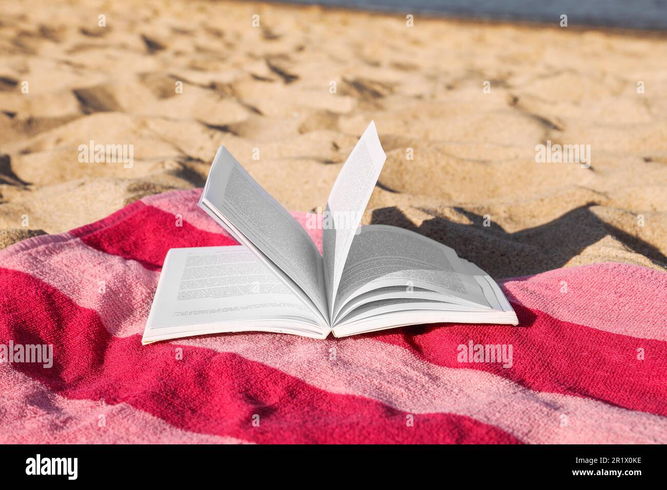 Beach towel and open book on sand near sea Stock Photo - Alamy