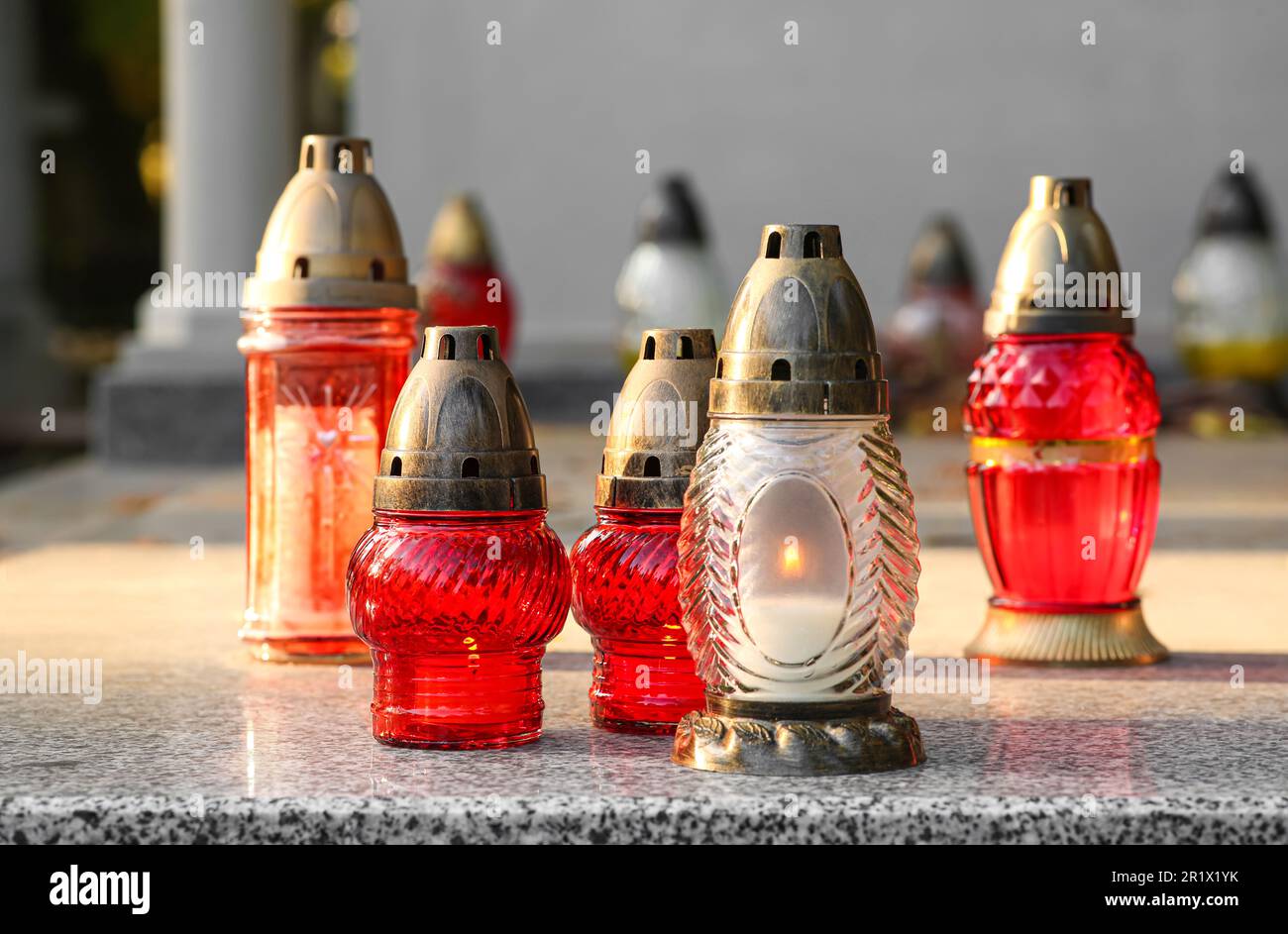 Different grave lanterns with burning candles on granite tombstone