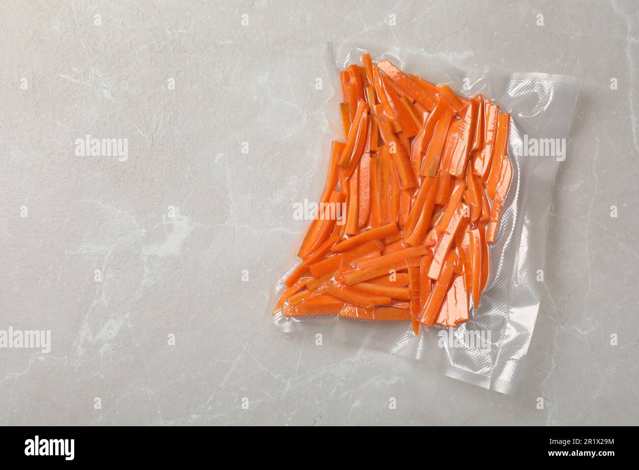 Vacuum packing with cut carrots on light grey marble table, top view