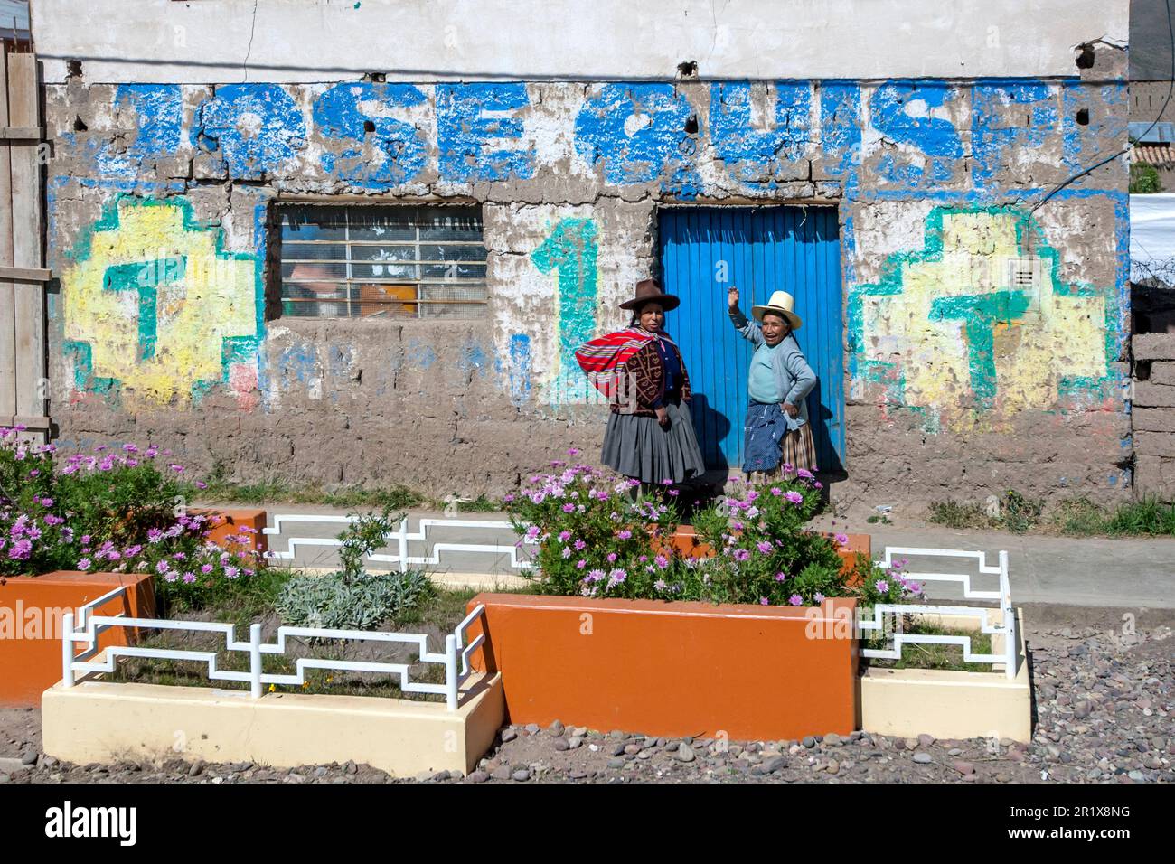 Peruvian women stand outside a colourfully painted building on the road from Cusco to Puno in Peru. Stock Photo