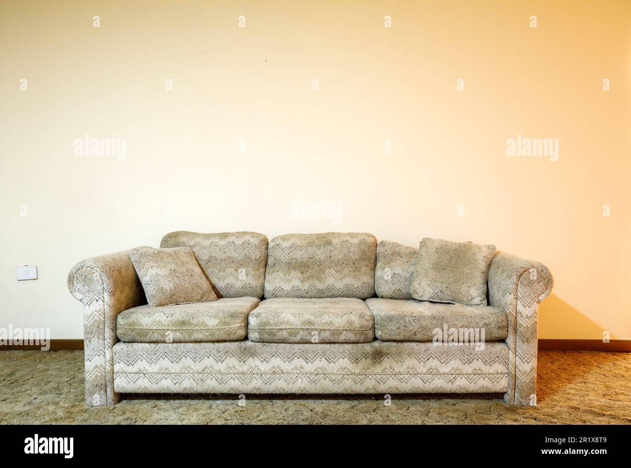 A dirty couch sitting in front of a starkly empty wall.  This house has since been demolished. Stock Photo