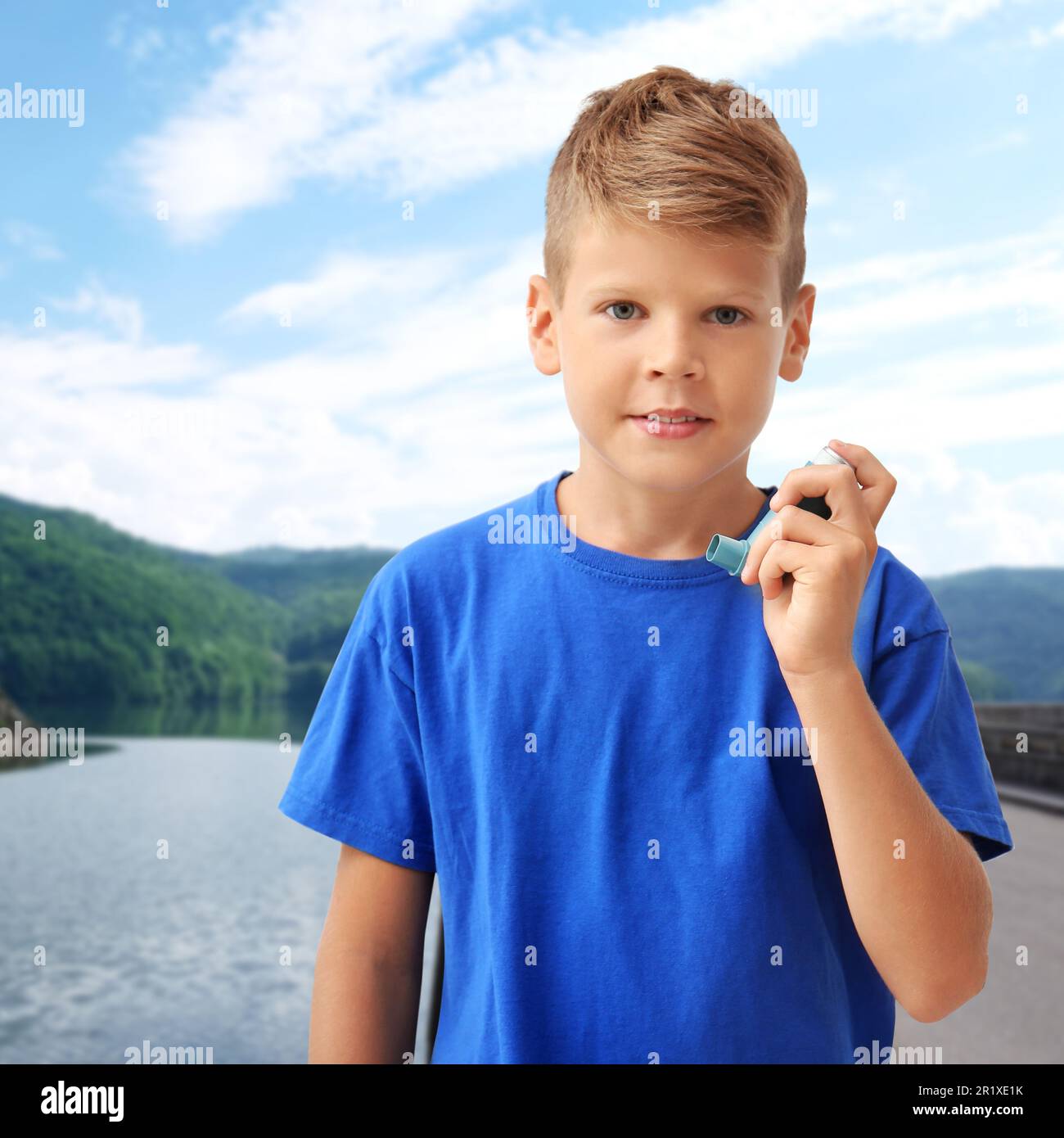 Little boy with asthma inhaler near lake. Emergency first aid during outdoor recreation Stock Photo