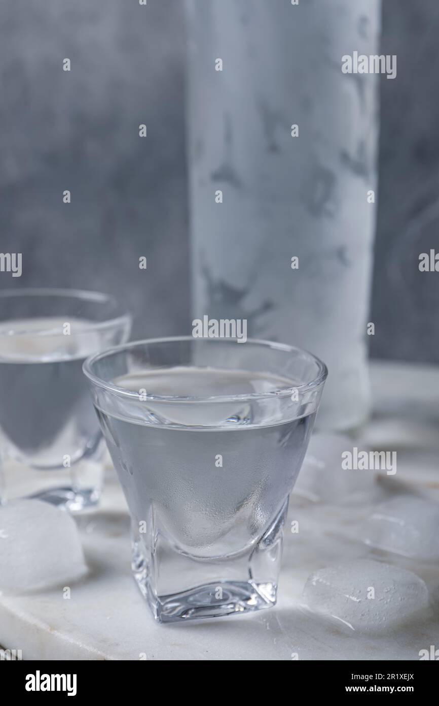 Shot glasses and bottle of vodka with ice cubes on table Stock Photo