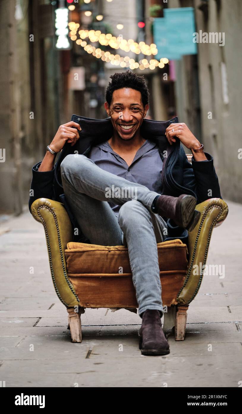 Black man looking at the camera and smiling while sitting on an armchair outdoors. Stock Photo