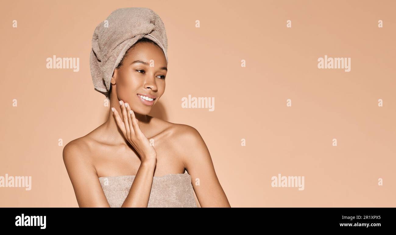 Body care concept. Happy African American woman with moisturized fresh skin with towel on head after bath procedures on beige background Stock Photo